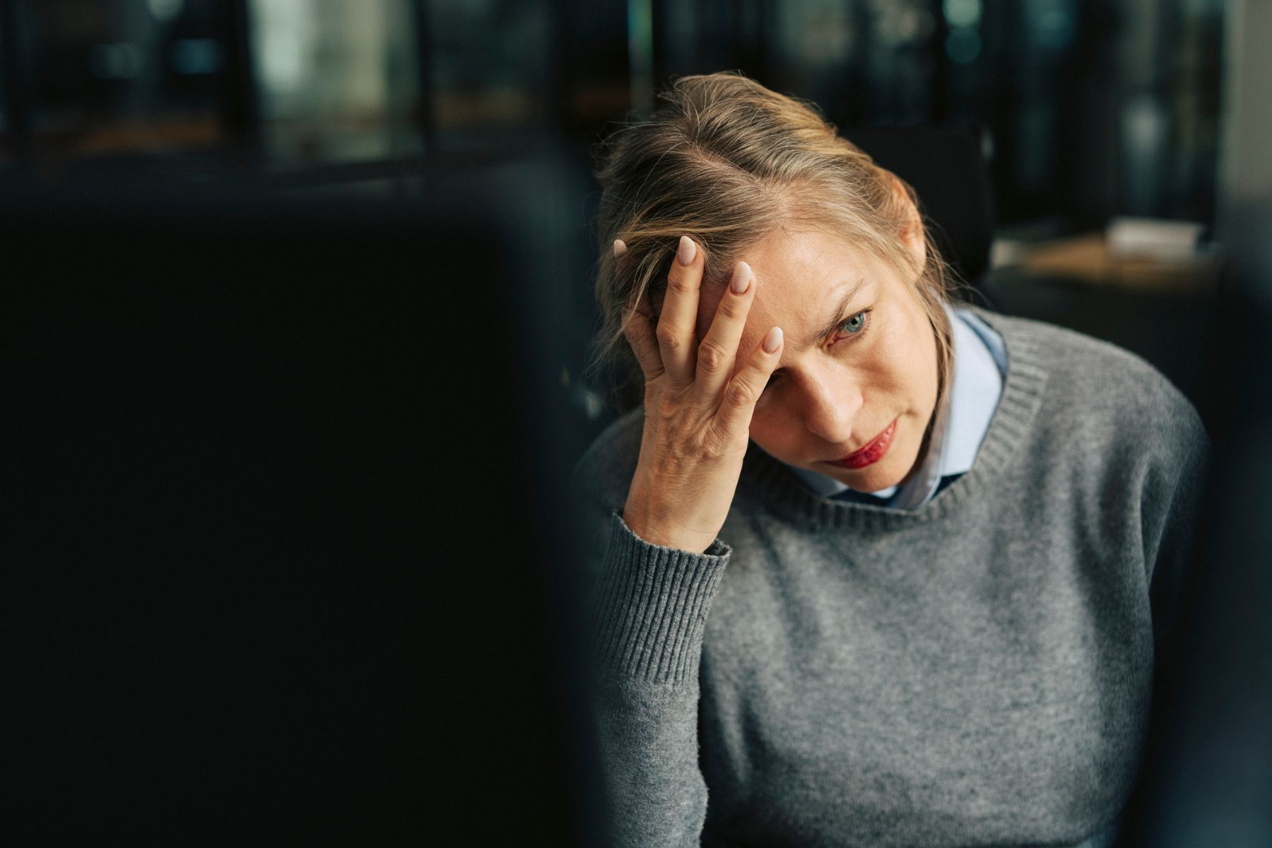 A woman in a dark room puts her head on her hand