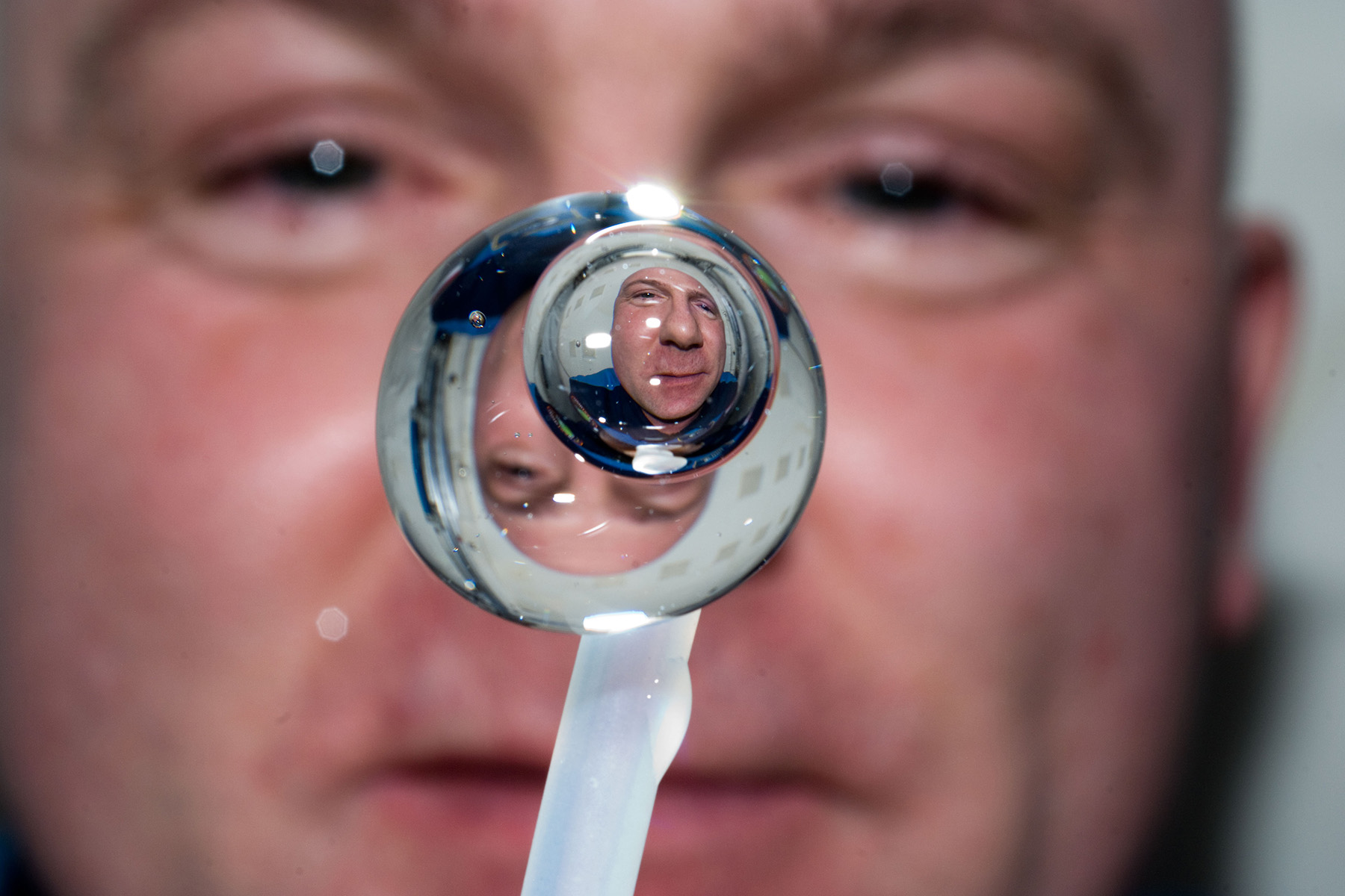 A bubble of water with a bubble of air inside floating in space. A man's face is distorted inside the water