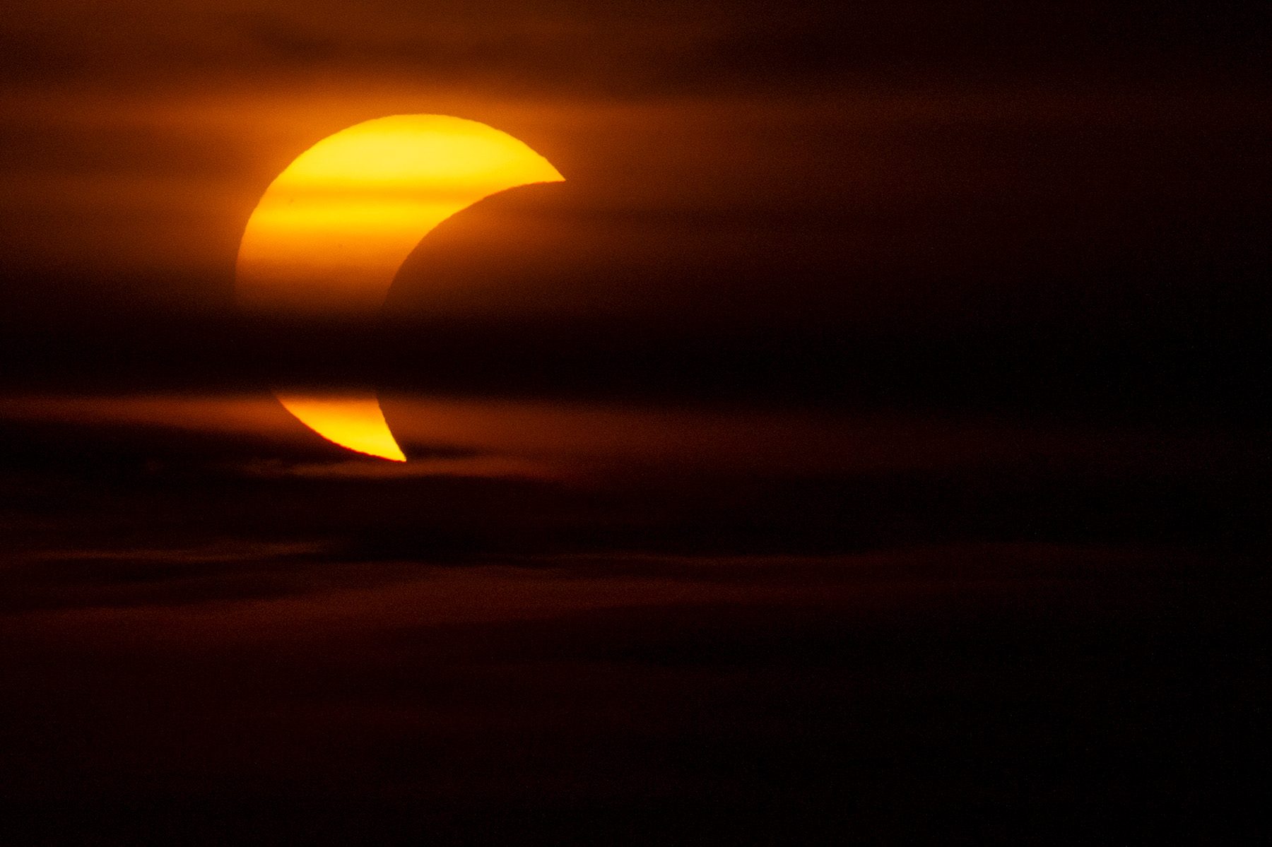Crescent sun partially obscured by clouds