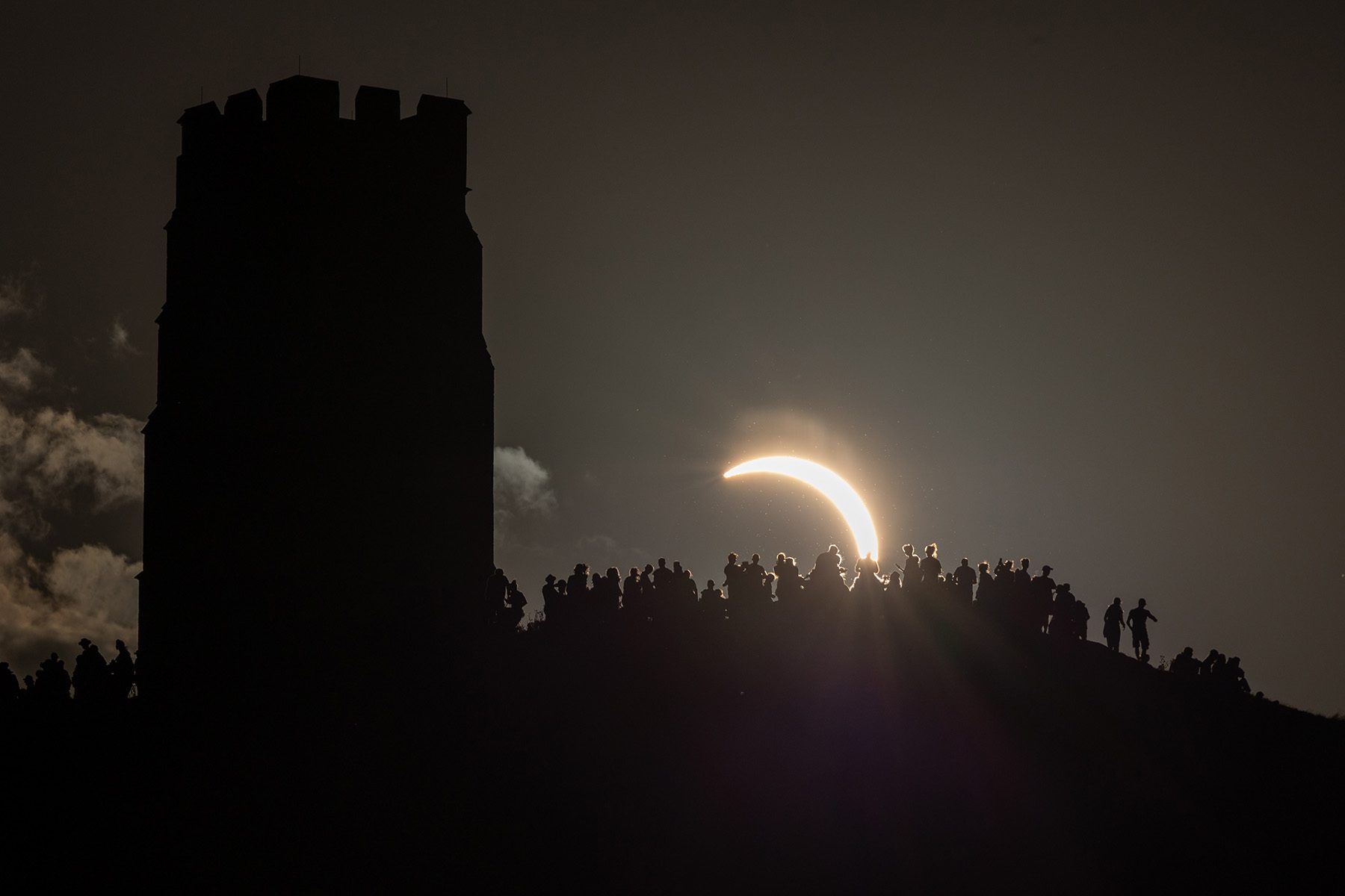 group of people watching the crescent of the sun, which appears much larger than normal in the distance