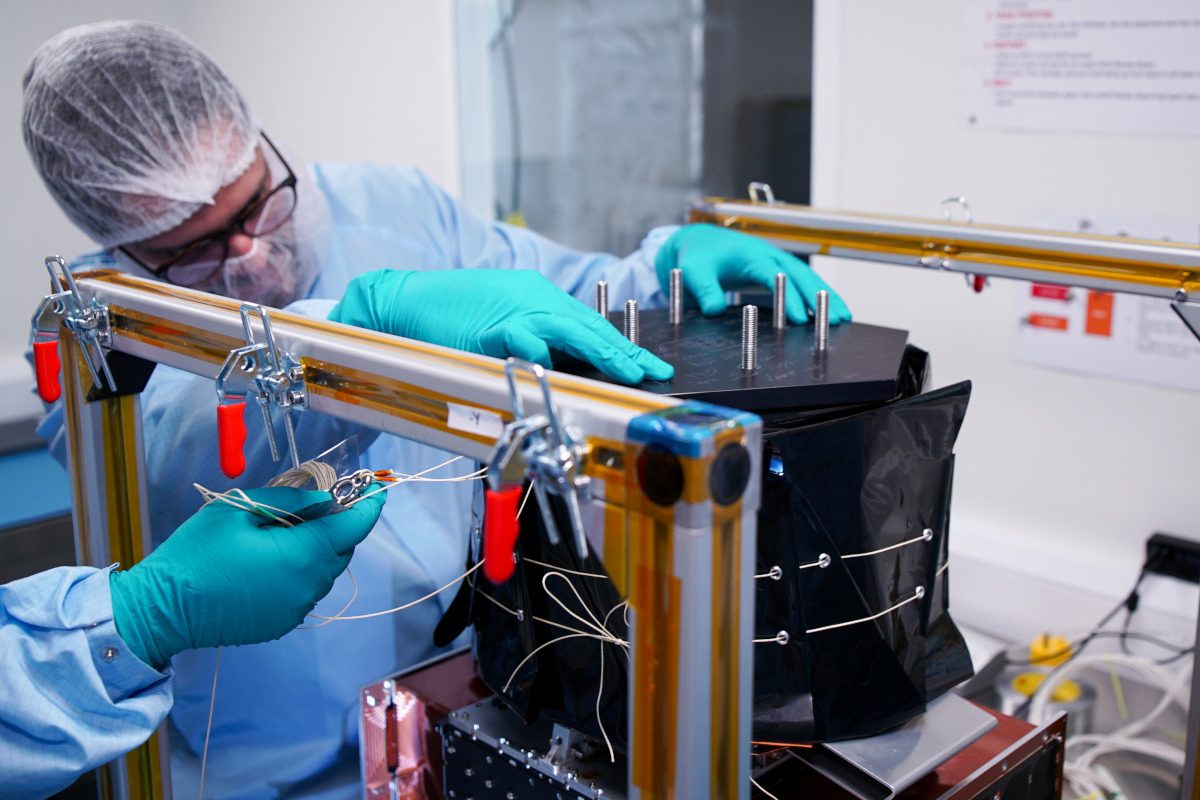 A scientist wearing protective gear is inspecting a black machine, the ForgeStar-1