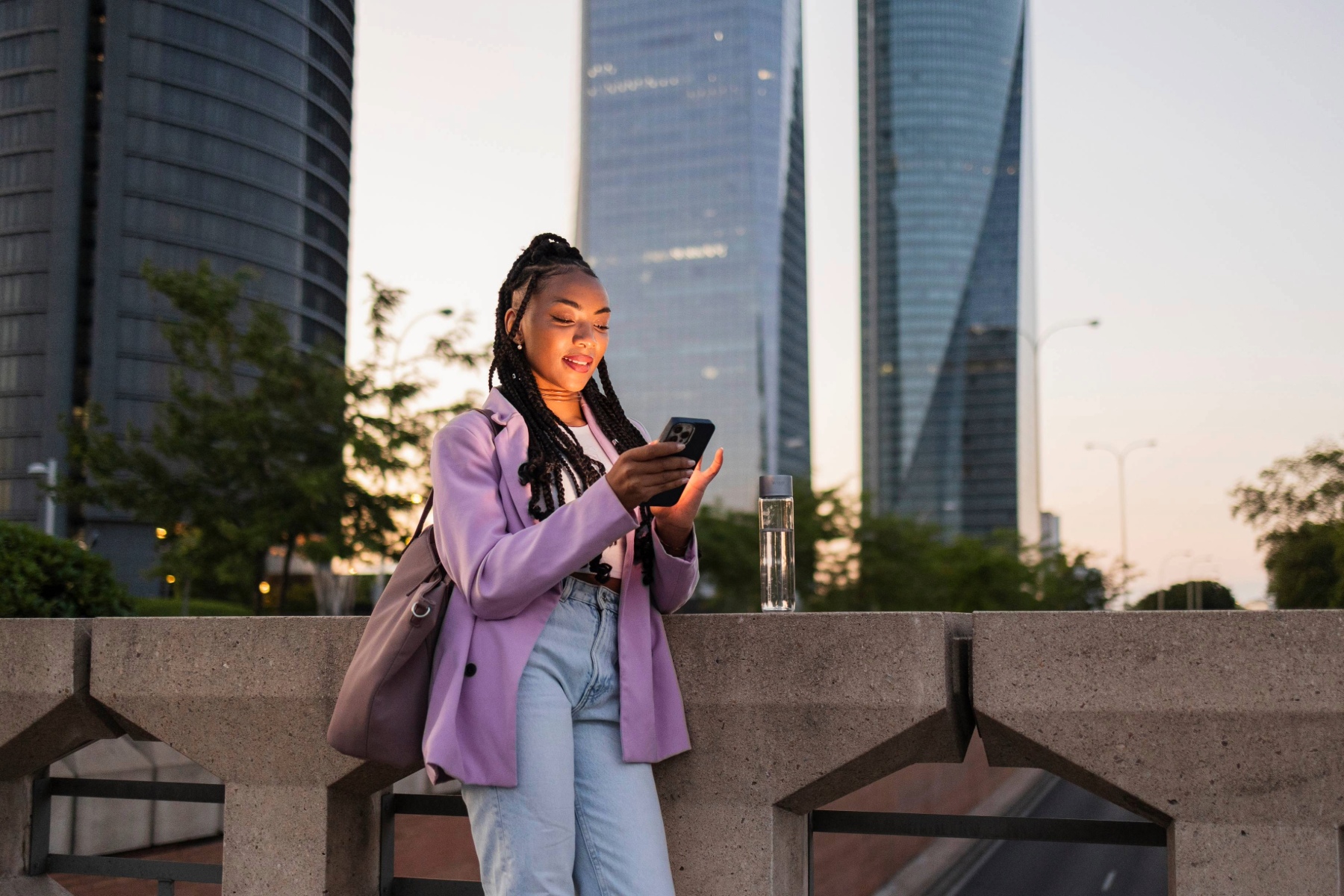 Young woman smiling looking down at her phone, with tall glass buildings in the background