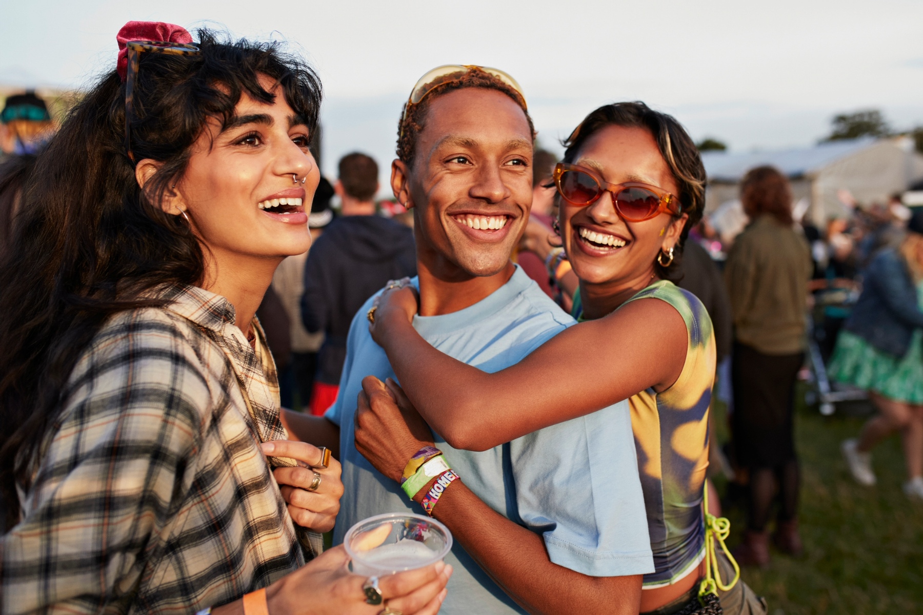 Three young people smiling, with one hugging the other from behind