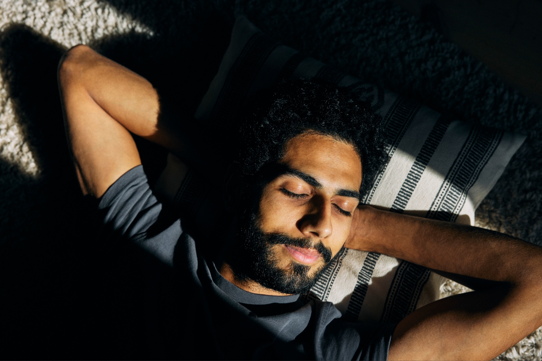 Young man in bed with his eyes closed and both hands behind his head