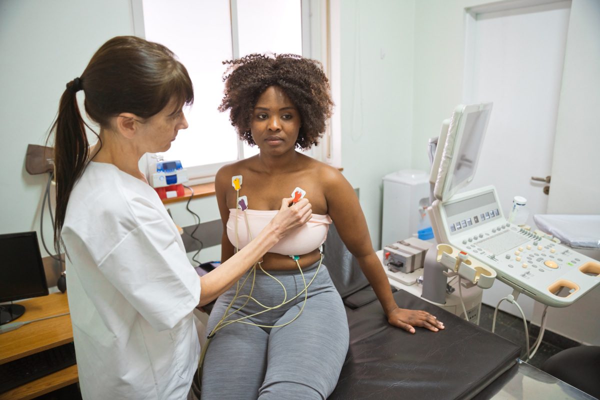 Female doctor placing electrodes on patient's breast during ecography test in examination room