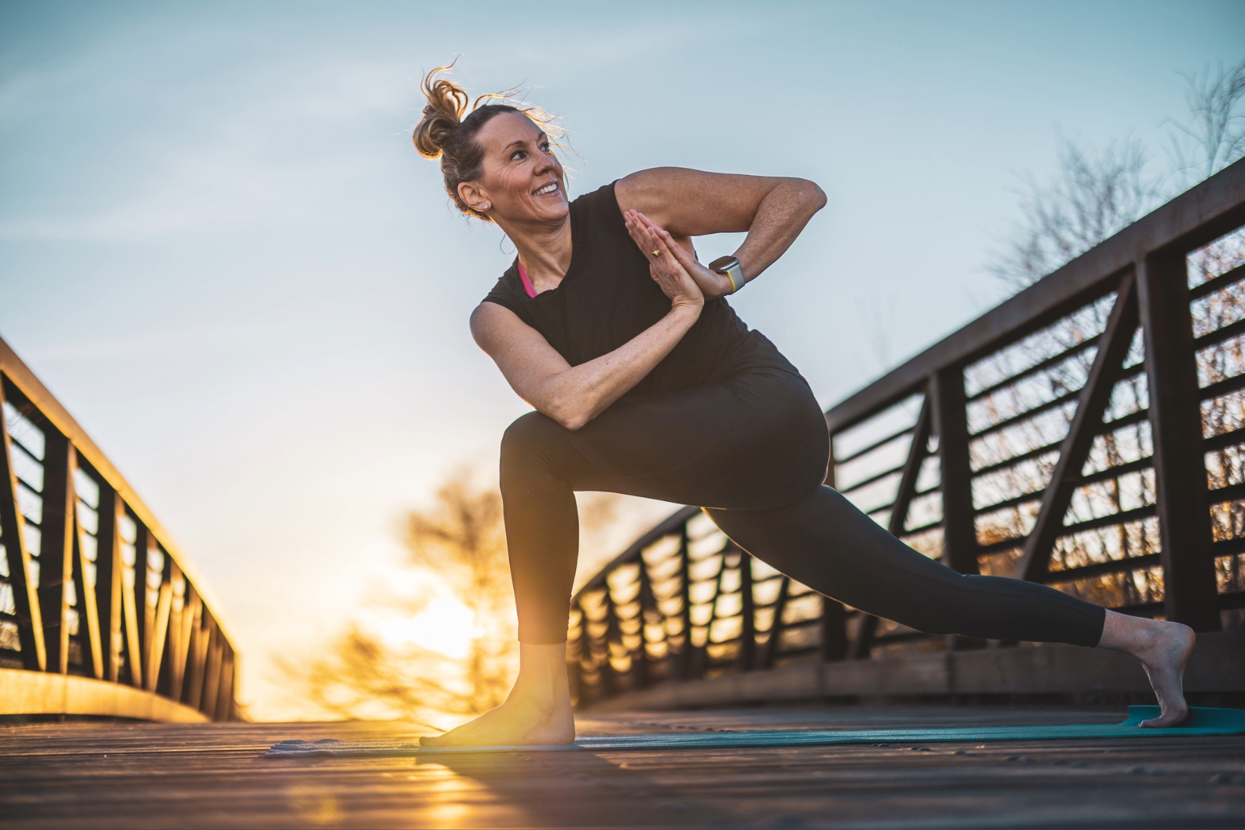 Woman outside on a bright day smiling and doing a side lunge