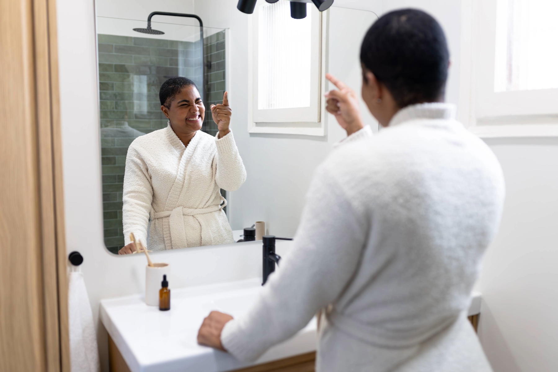 Woman looking, smiling and pointing at herself in the mirror