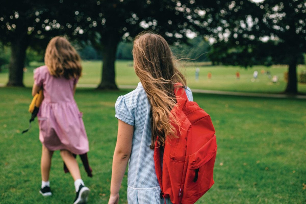 Two school children outside in a field with trees, other kids are blurred in the background