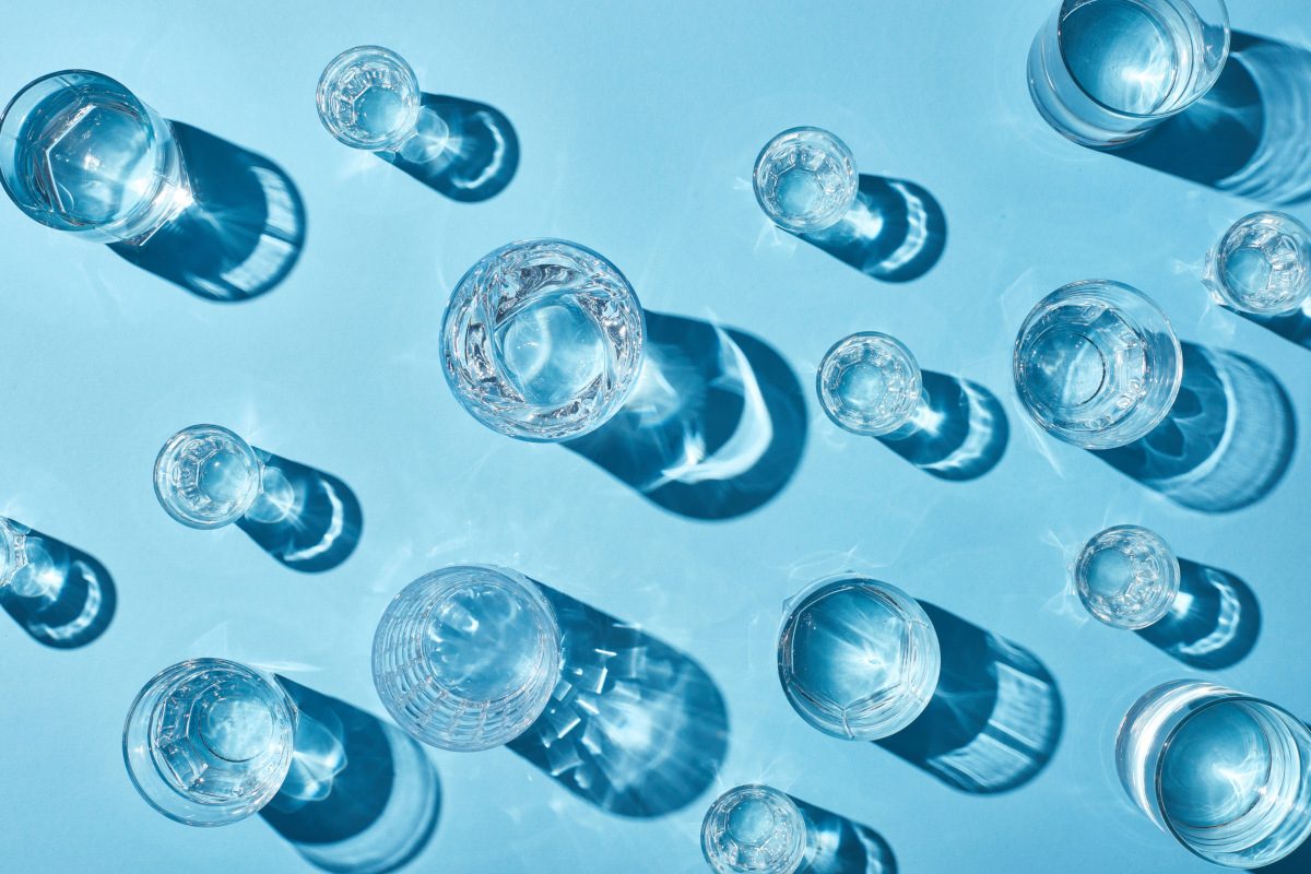 top view of transparent glasses with clear water and shadows on blue background
