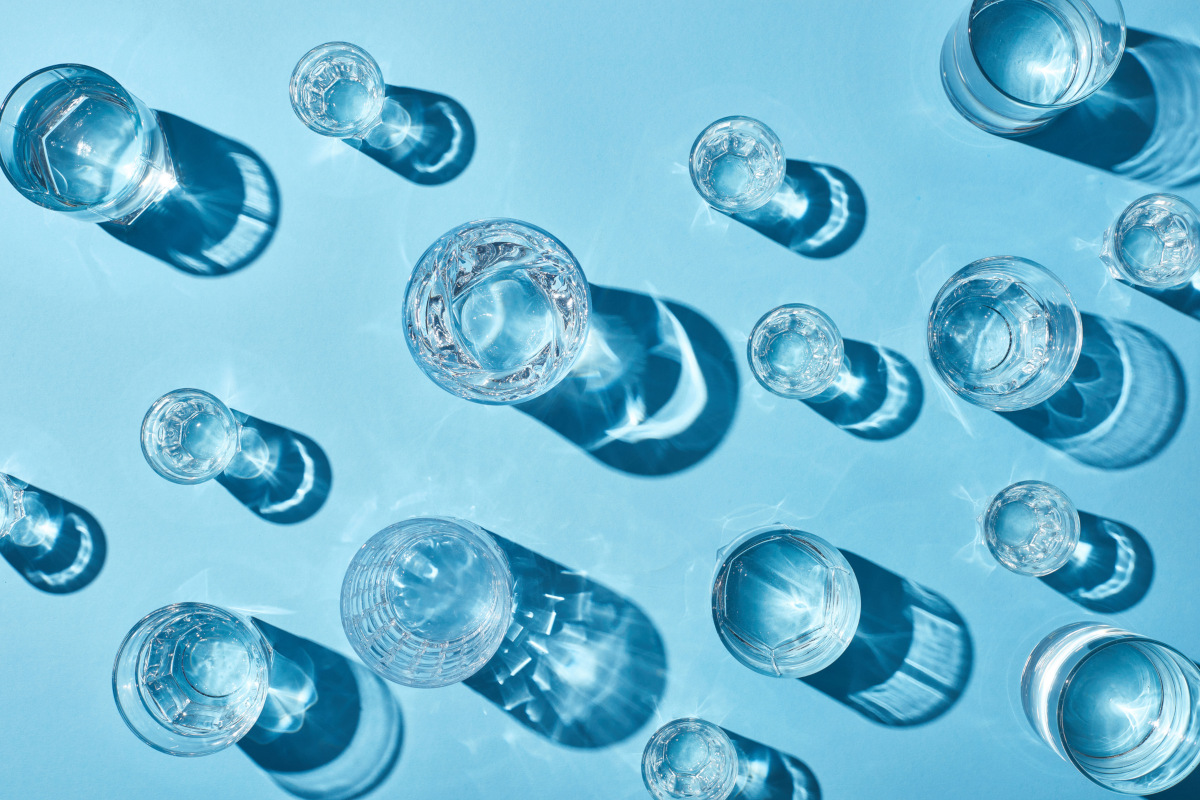 top view of transparent glasses with clear water and shadows on blue background