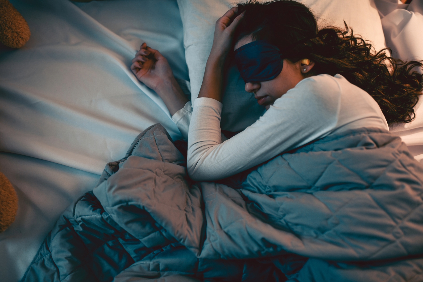Woman sleeping in bed wearing eye mask.