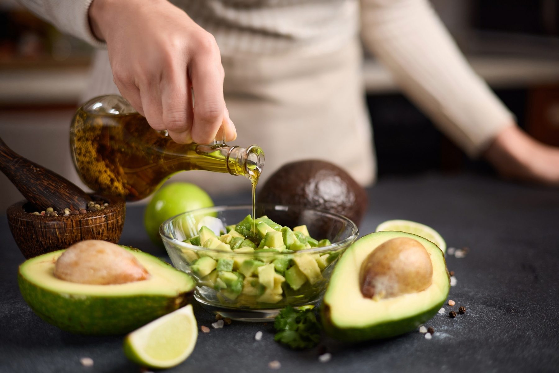 Person drizzling olive oil over chopped avocado