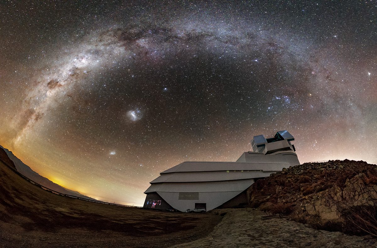 A low wide-angle shot of the vera rubin telescope with an arching milkyway and star-lit sky going directly over the top of it.