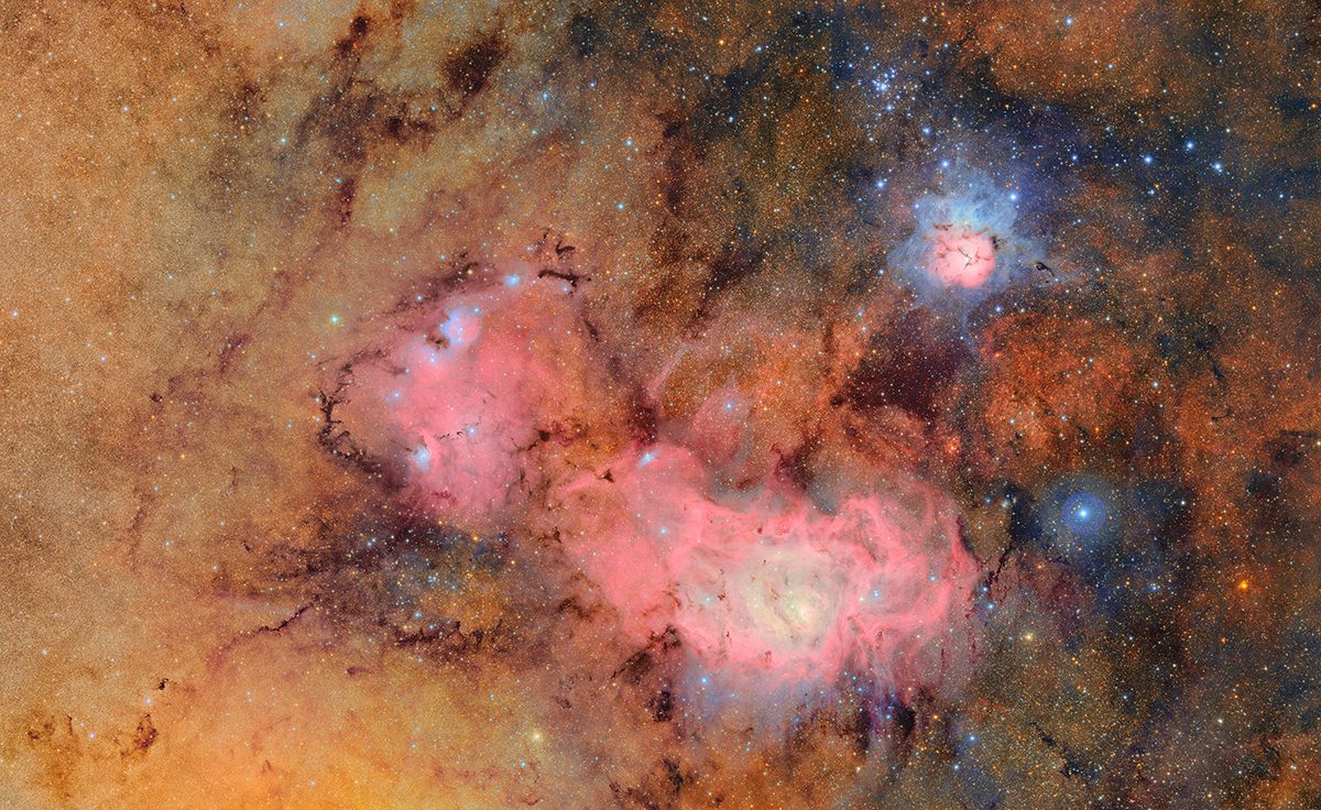 A pink nebula sits amongst a star filled orange background.