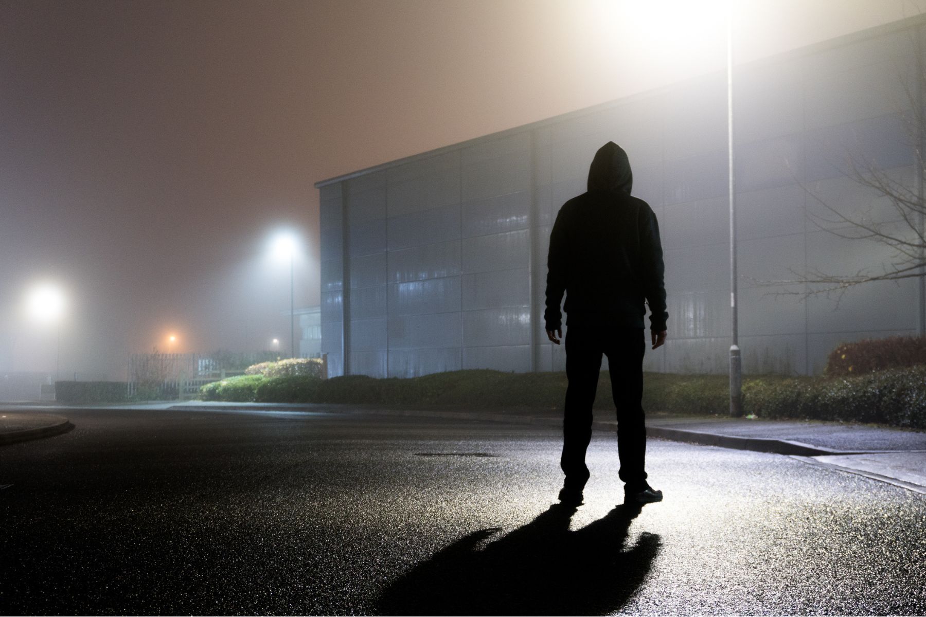 A mysterious figure stands in a shadowy car park