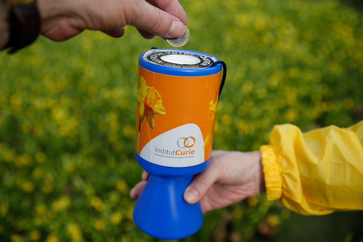 Close up of a person putting a pound coin into a charity donation bucket