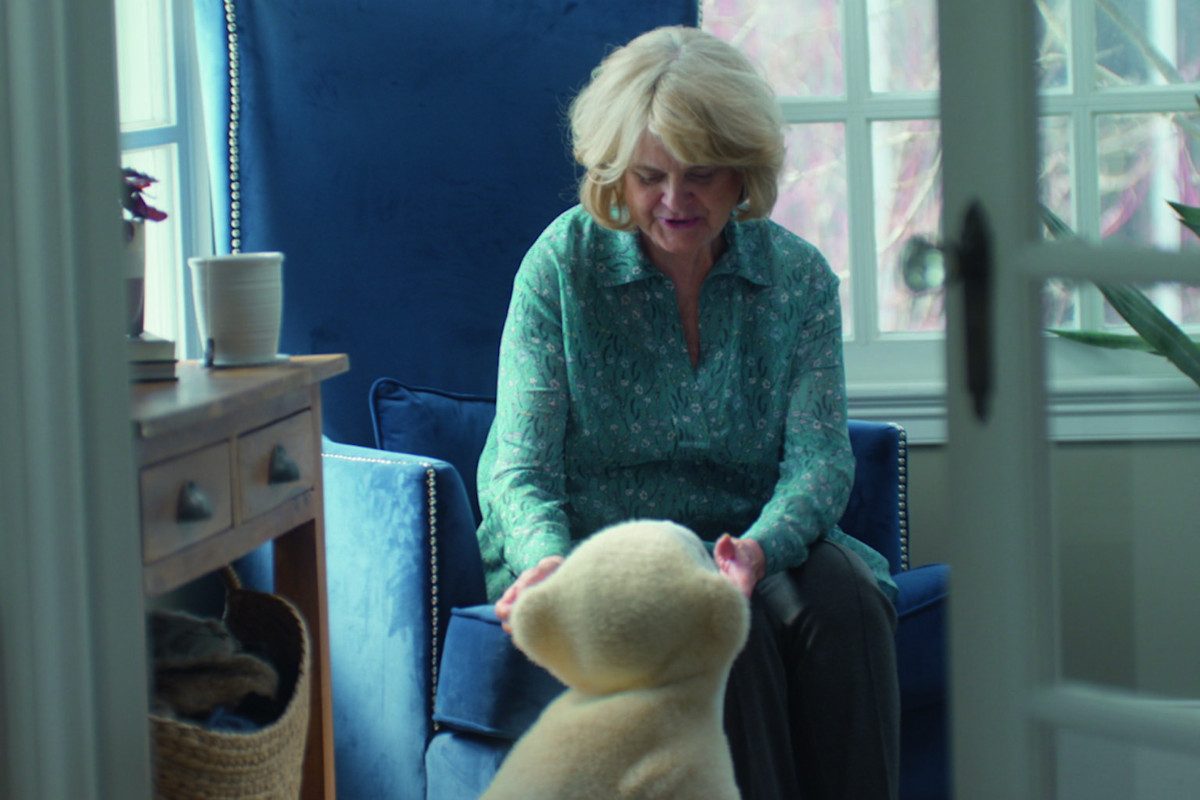 Photo of an elderly person sat in an armchair, looking down at a Familiar robot