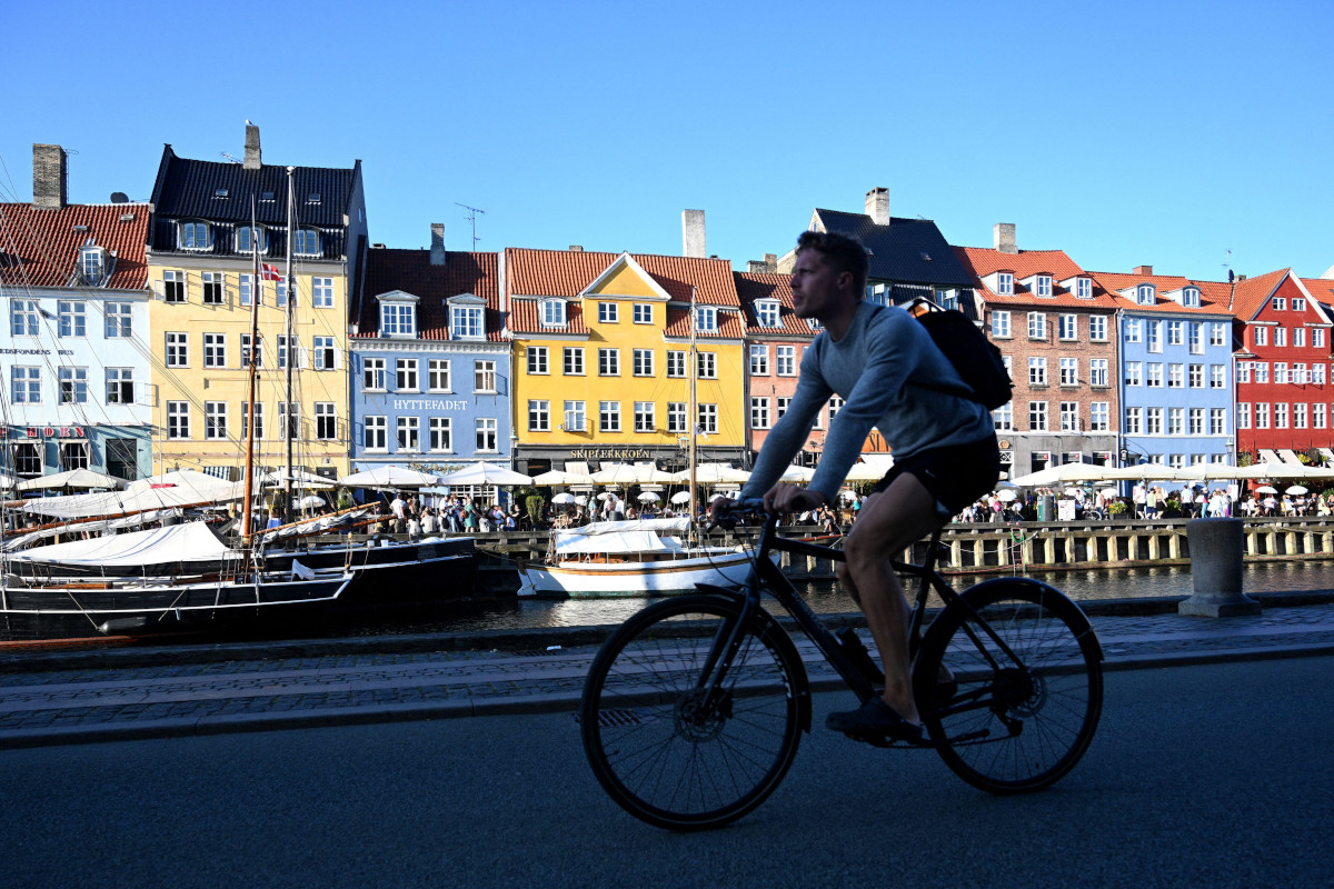 A person cycling alongside a river, multi-coloured houses are on the other side of the river