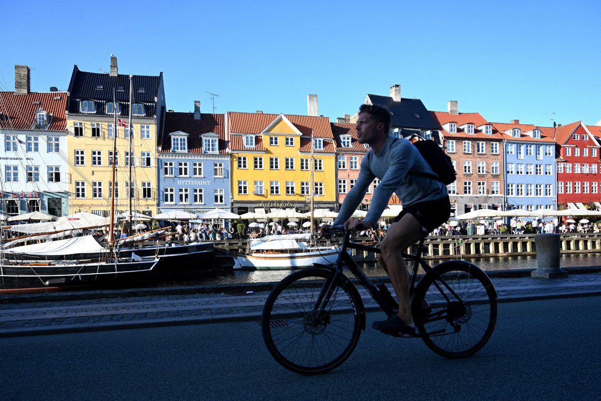 A person cycling alongside a river, multi-coloured houses are on the other side of the river