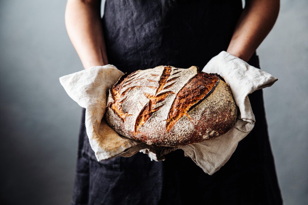 Photo of a person holding a freshly-baked loaf of sourdough bread.