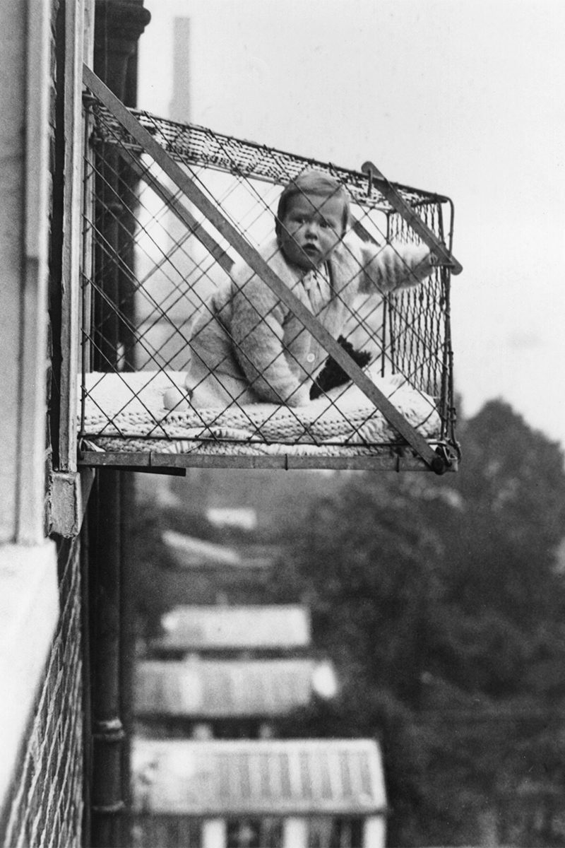 Baby in cage hanging out of window.