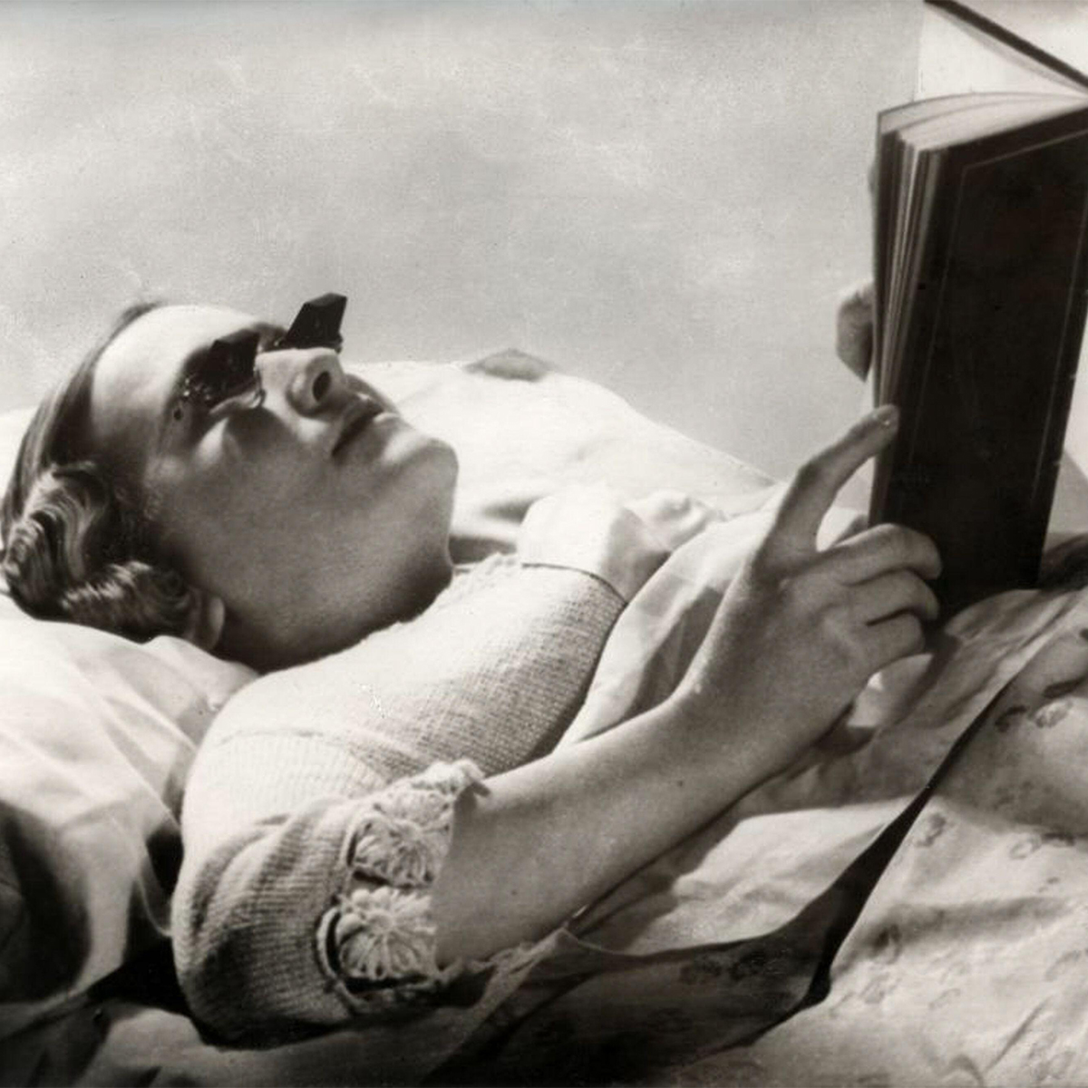 Woman lying Down reading book with weird glasses.