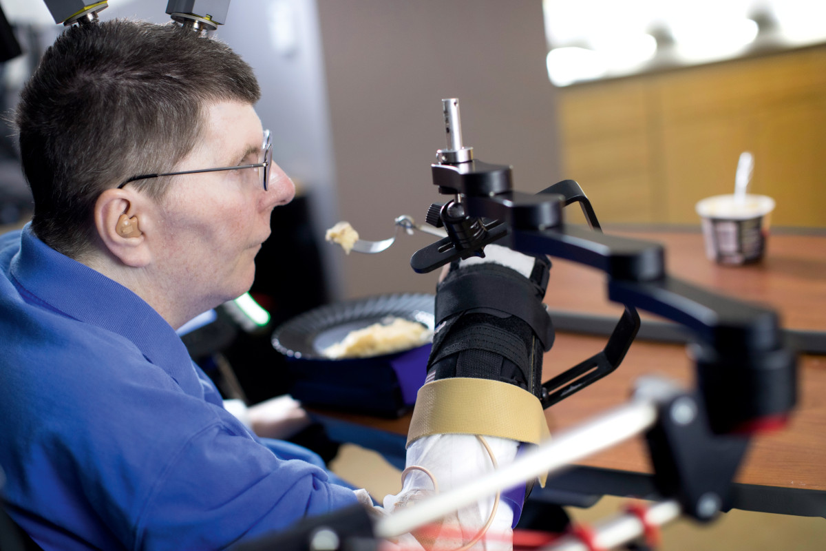 A person using a brain control interface to lift food to their face