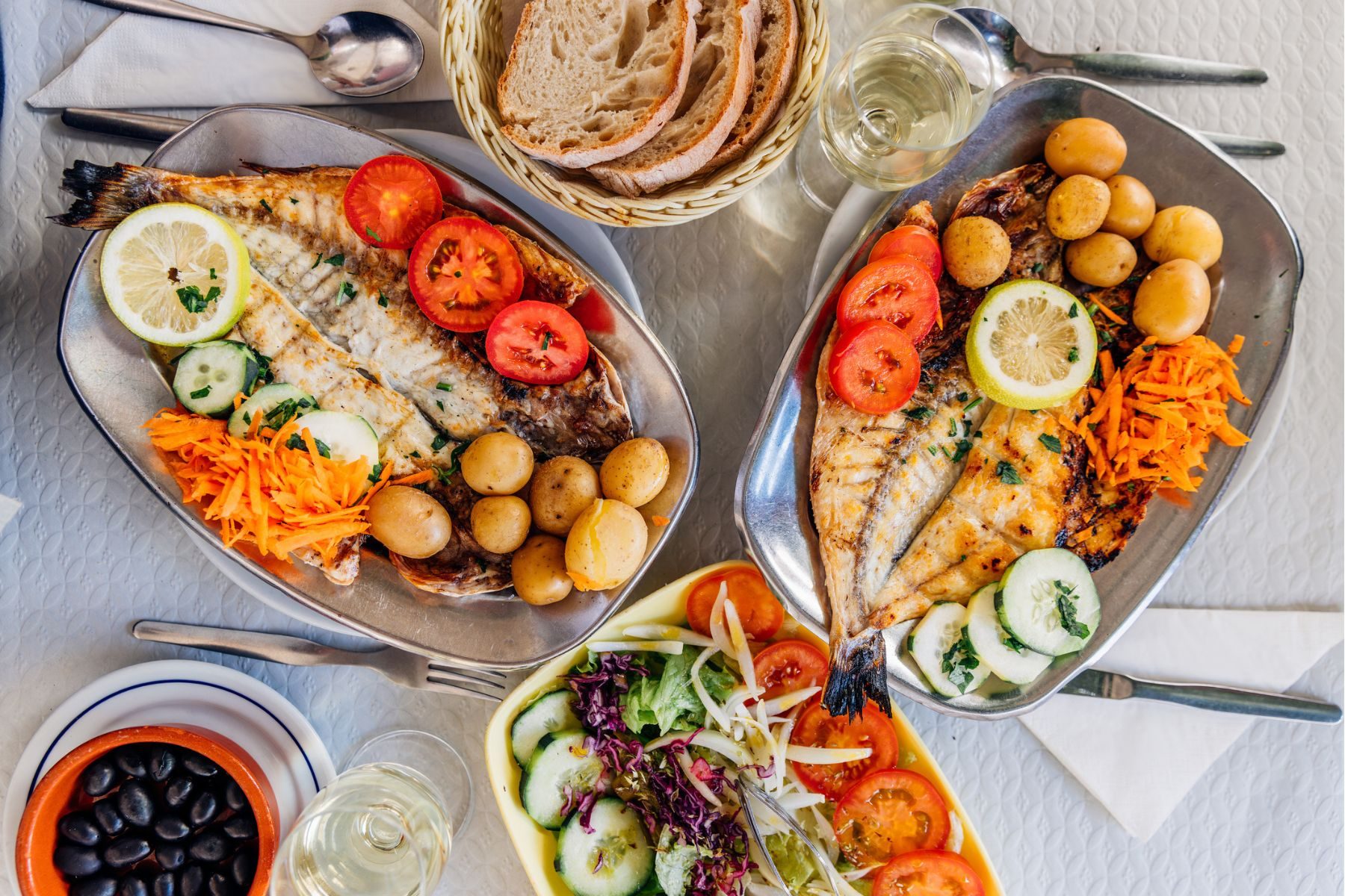 A table laid with Portuguese food, including fish, potatoes, vegetables, bread and olives