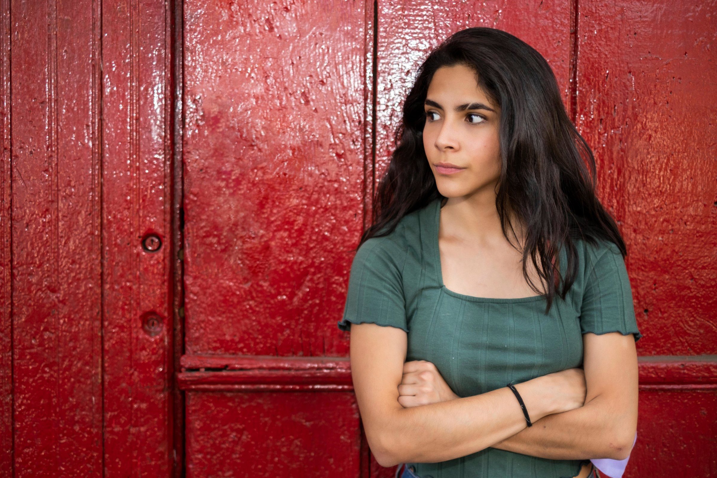 Woman standing with arms folded against large red door.