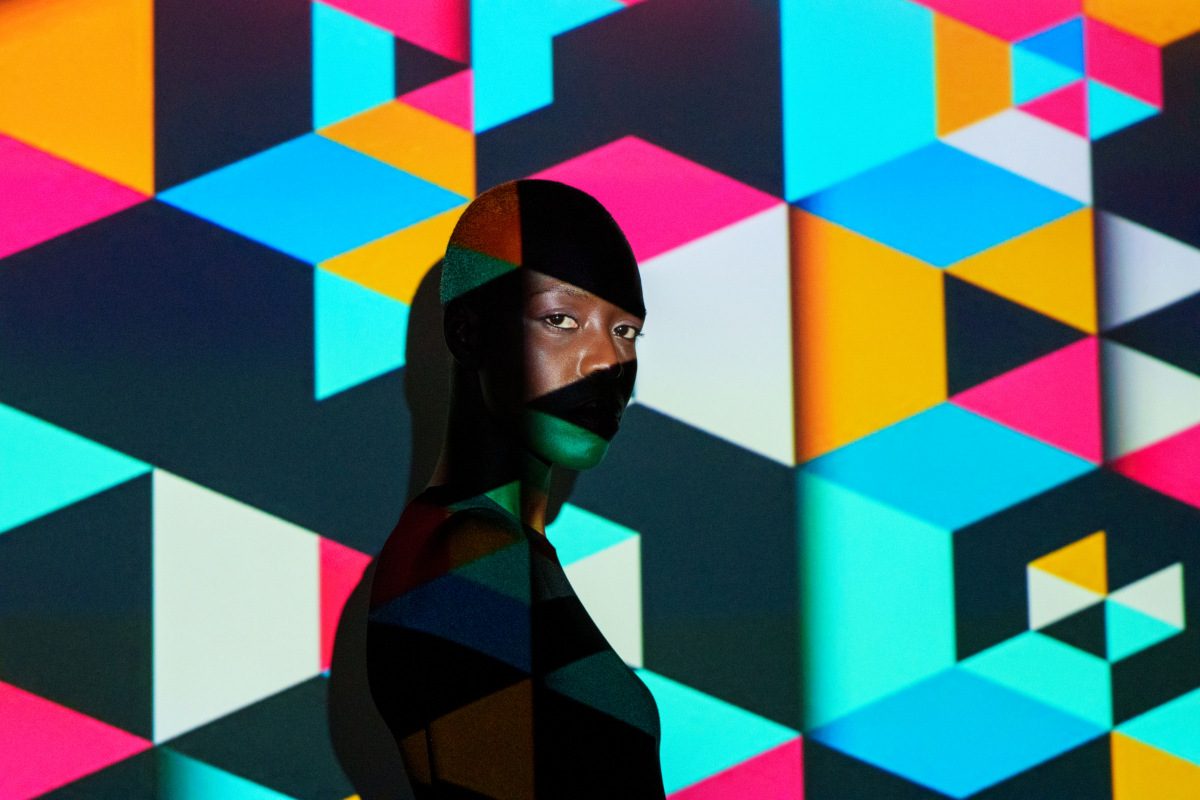 Young woman with projected geometric shapes on her face and body, creating an artistic and colorful portrait