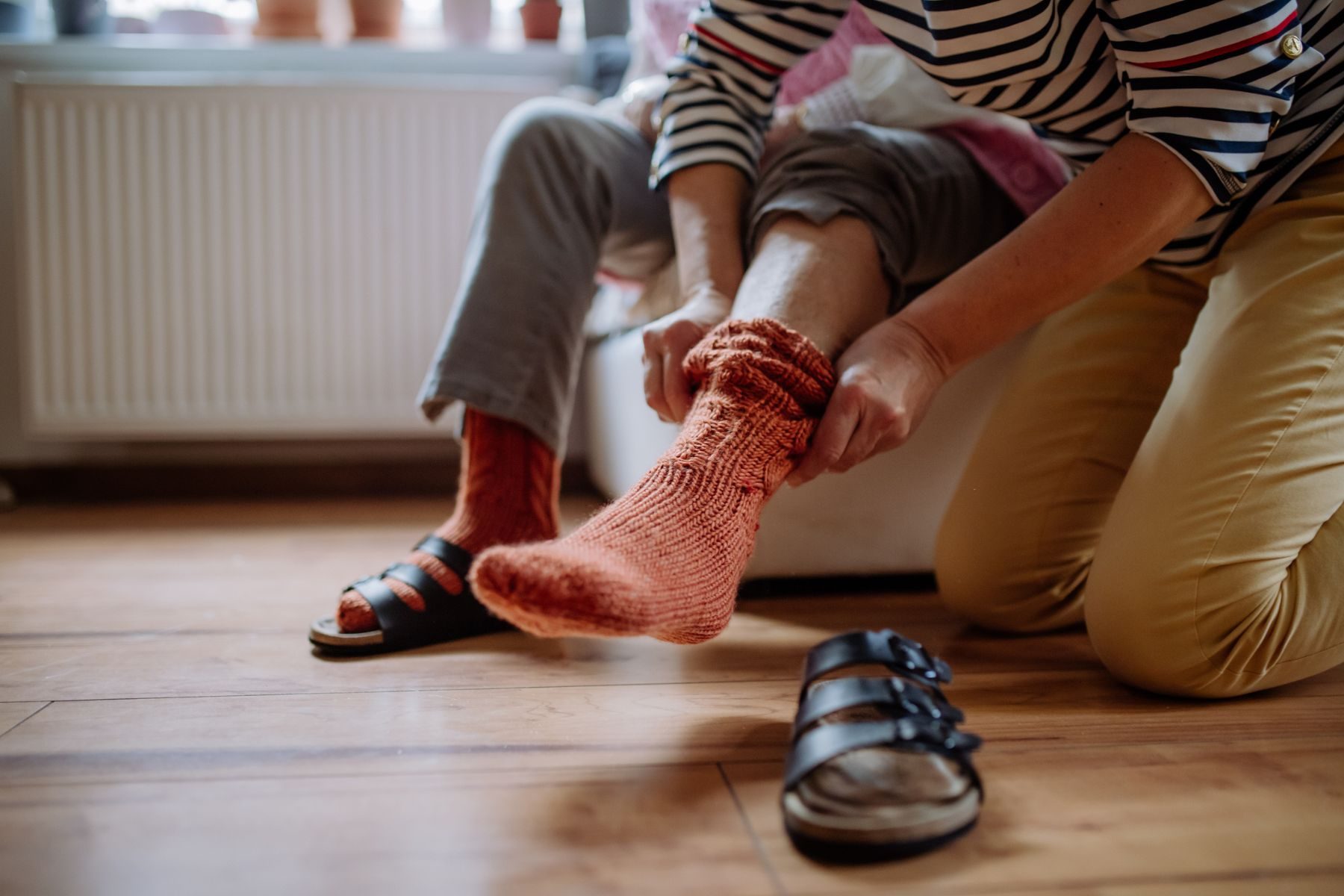 An elderly person has help putting on a sock