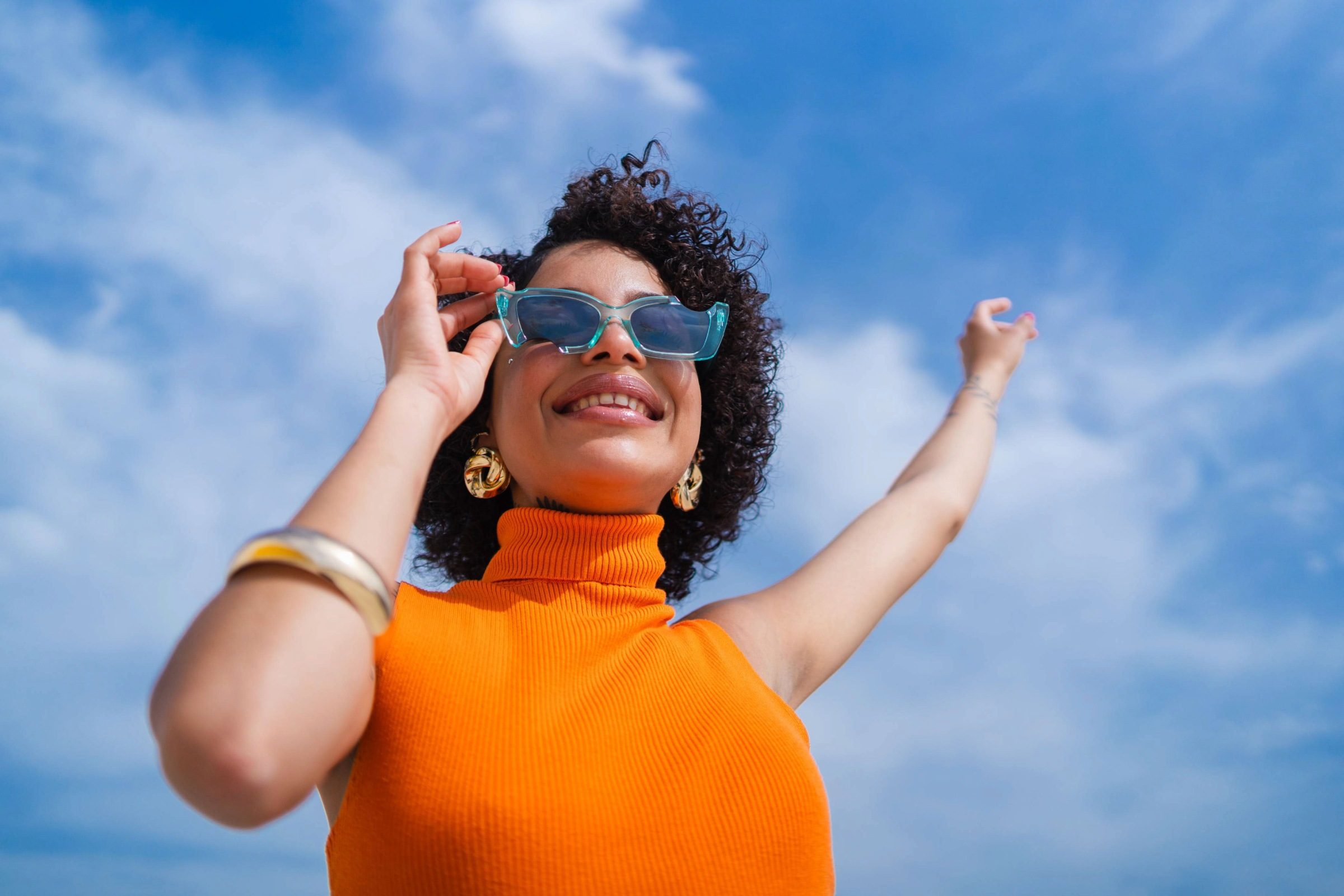 Woman in orange jumping smiling on a sunny day.