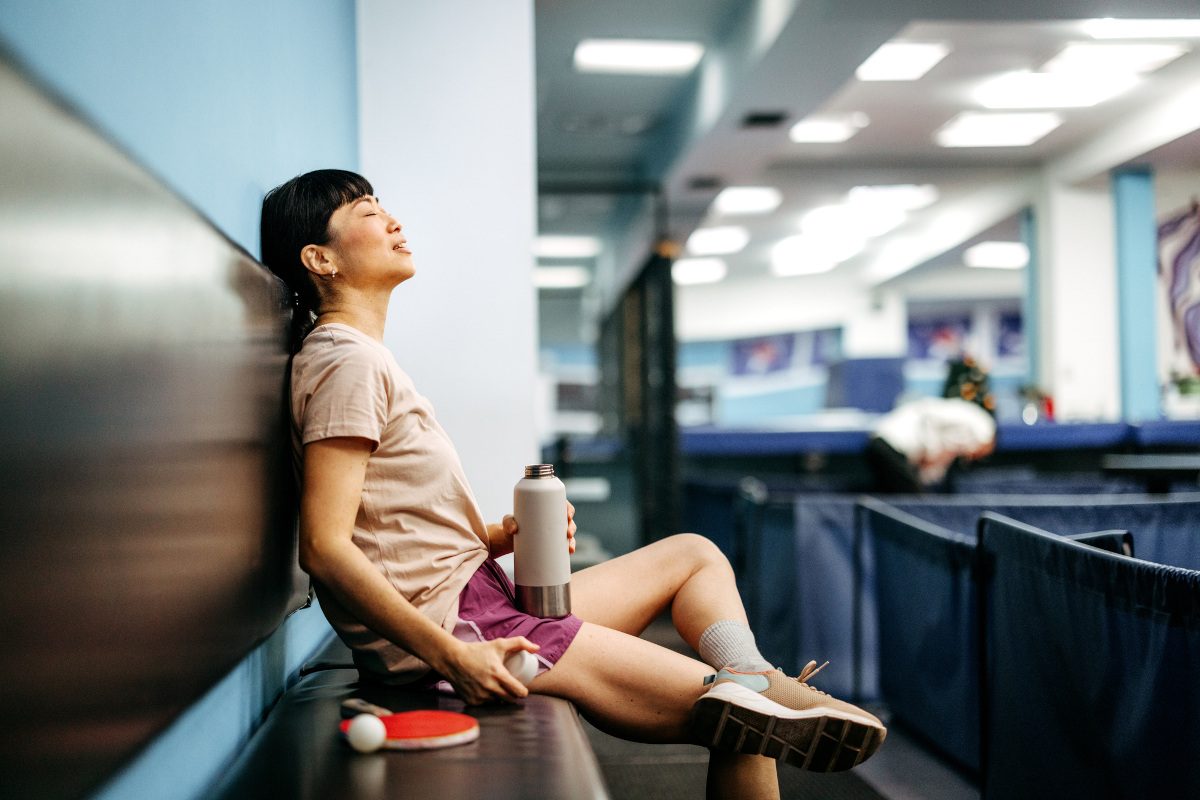 A woman sits on a bench in a table tennis gym, resting and relaxing after a session