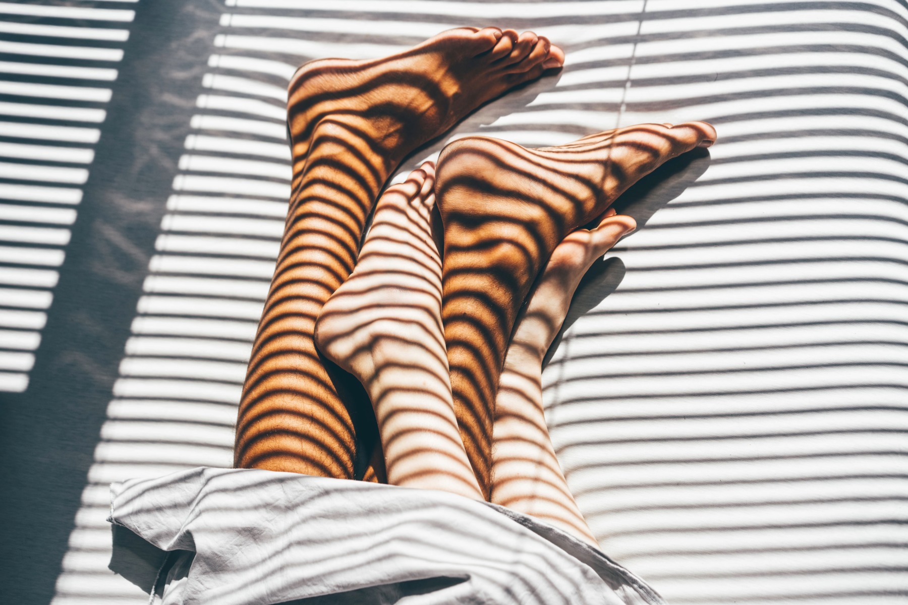Two people's feet crossing in bed.