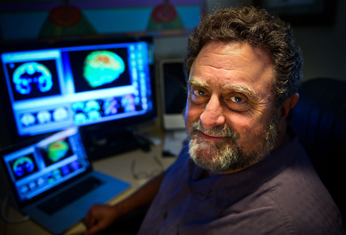 A man sits in front of screens with brain scans on them.