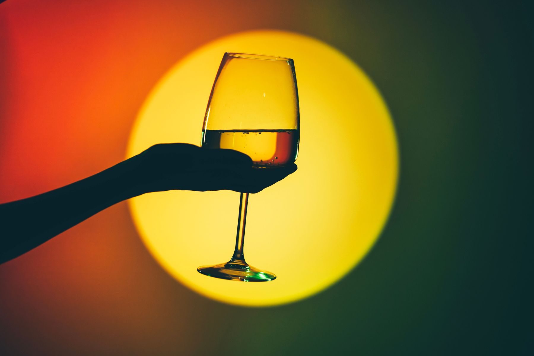 A hand holds a glass of wine in front of a yellow circle of light