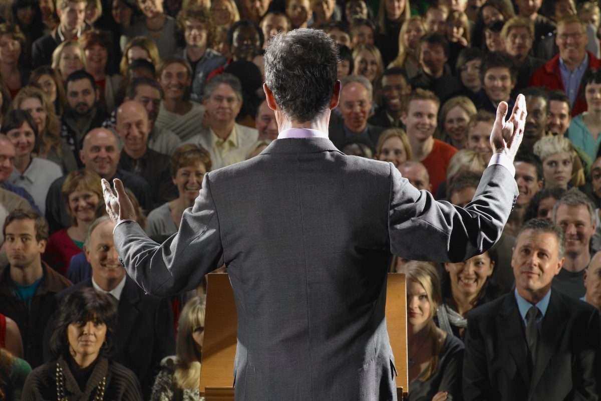 A person addressing a happy crowd with their back to the camera.