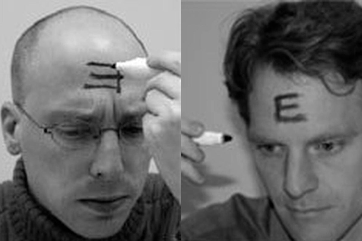 Two black and white photos of people drawing the letter 'E' on their forehead. The E on the left is backwards.