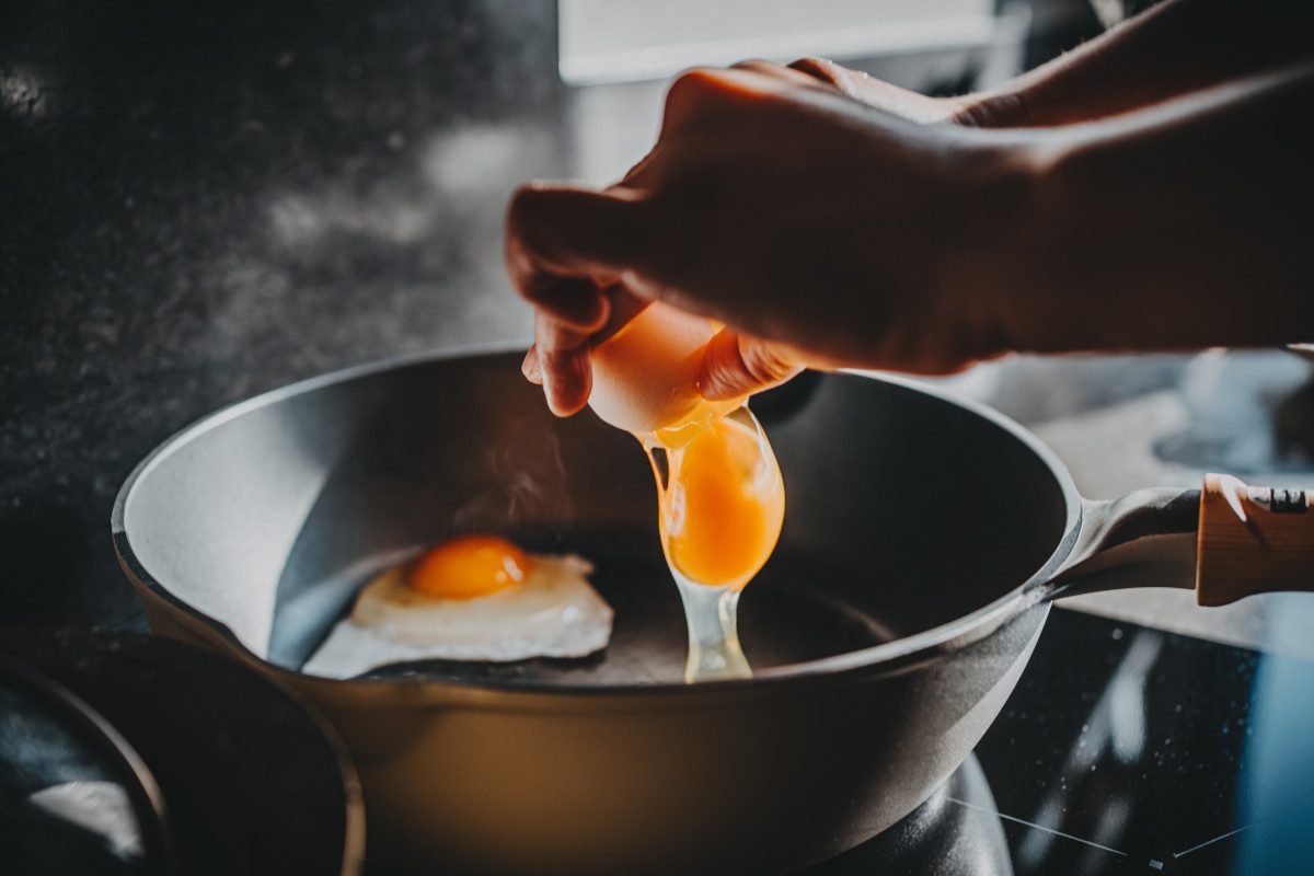 Close-up of a hand cracking an egg into a sizzling frying pan 