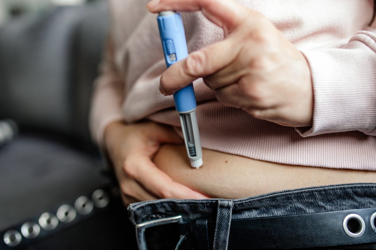 Woman subcutaneously self-injecting semaglutide pen into abdomen