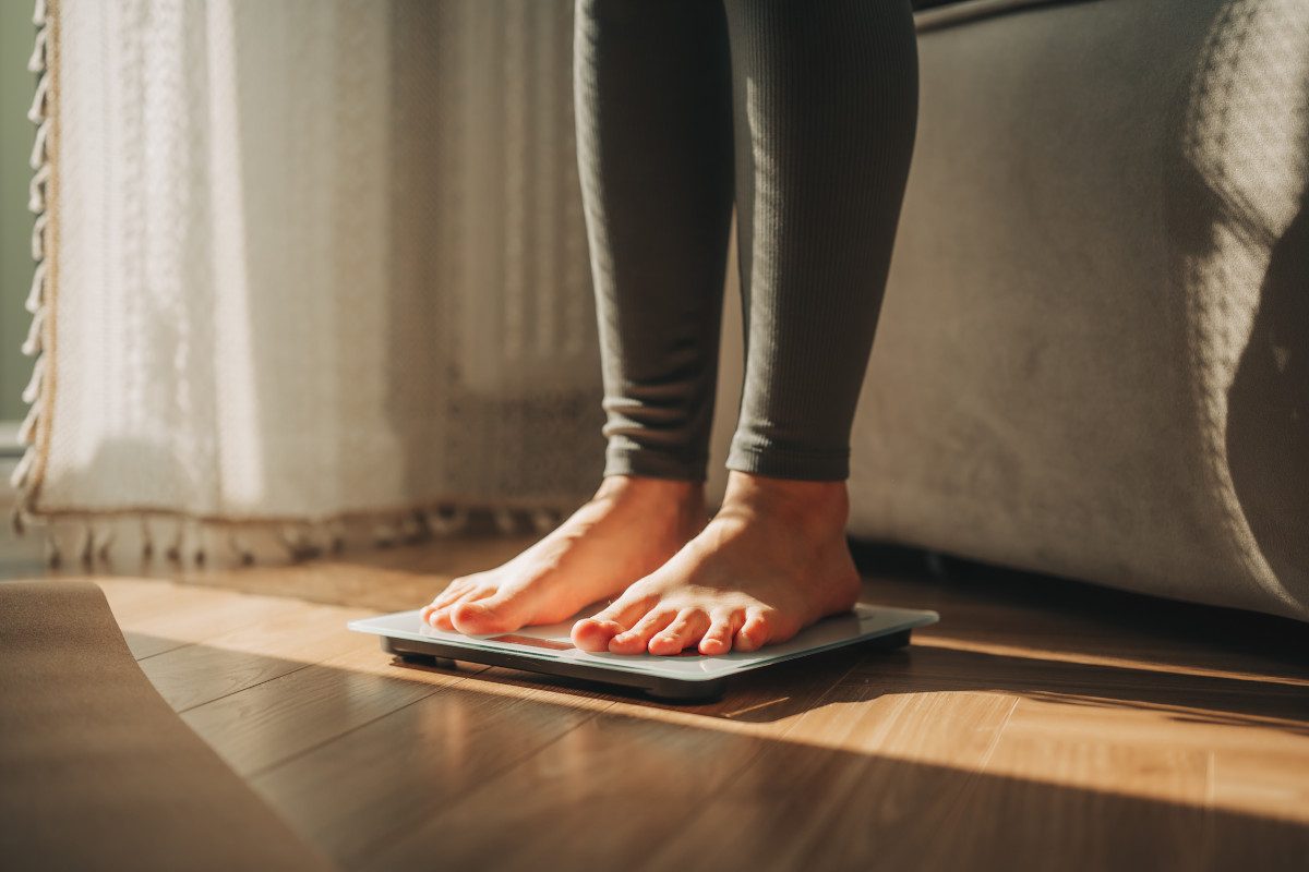Legs of young woman standing on scale to measure weight in white room