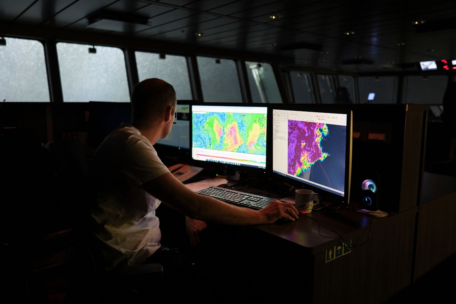 A man sits in the dark at a desk inside a boat, looking at thermal imaging maps