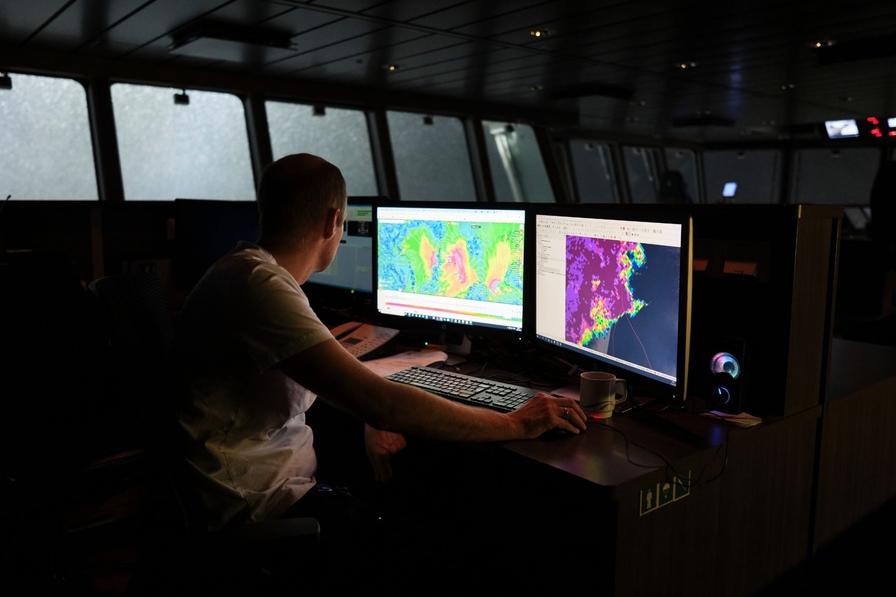 A man sits in the dark at a desk inside a boat, looking at thermal imaging maps