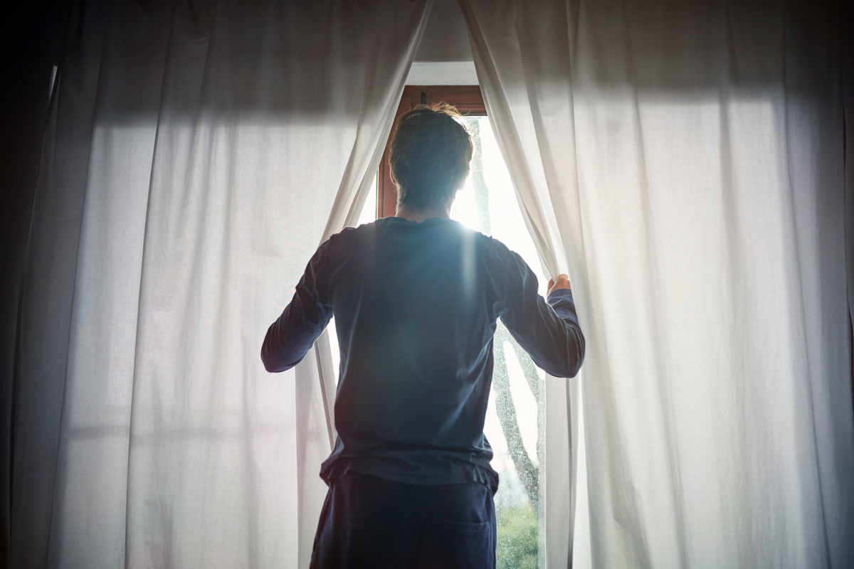 Man opening curtains on a sunny day