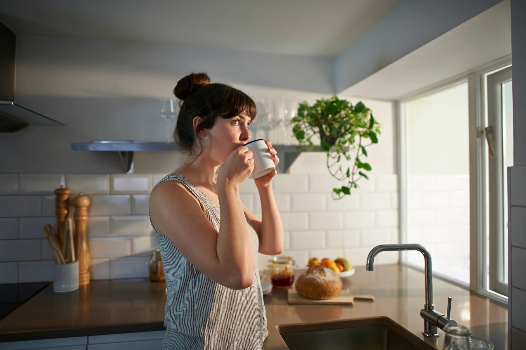 Woman drinking coffee in morning in kitchen.
