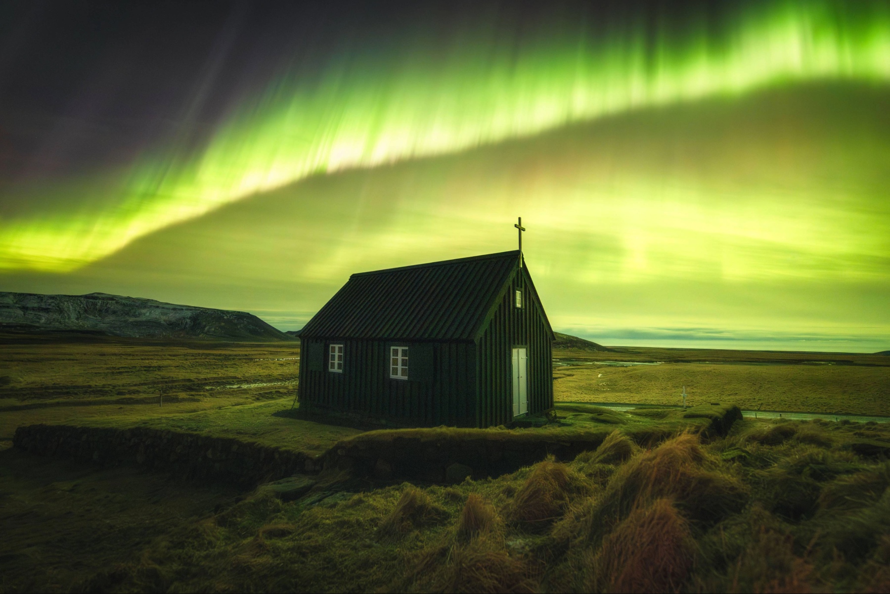 Green lights spread across the sky above a church in the middle of a field