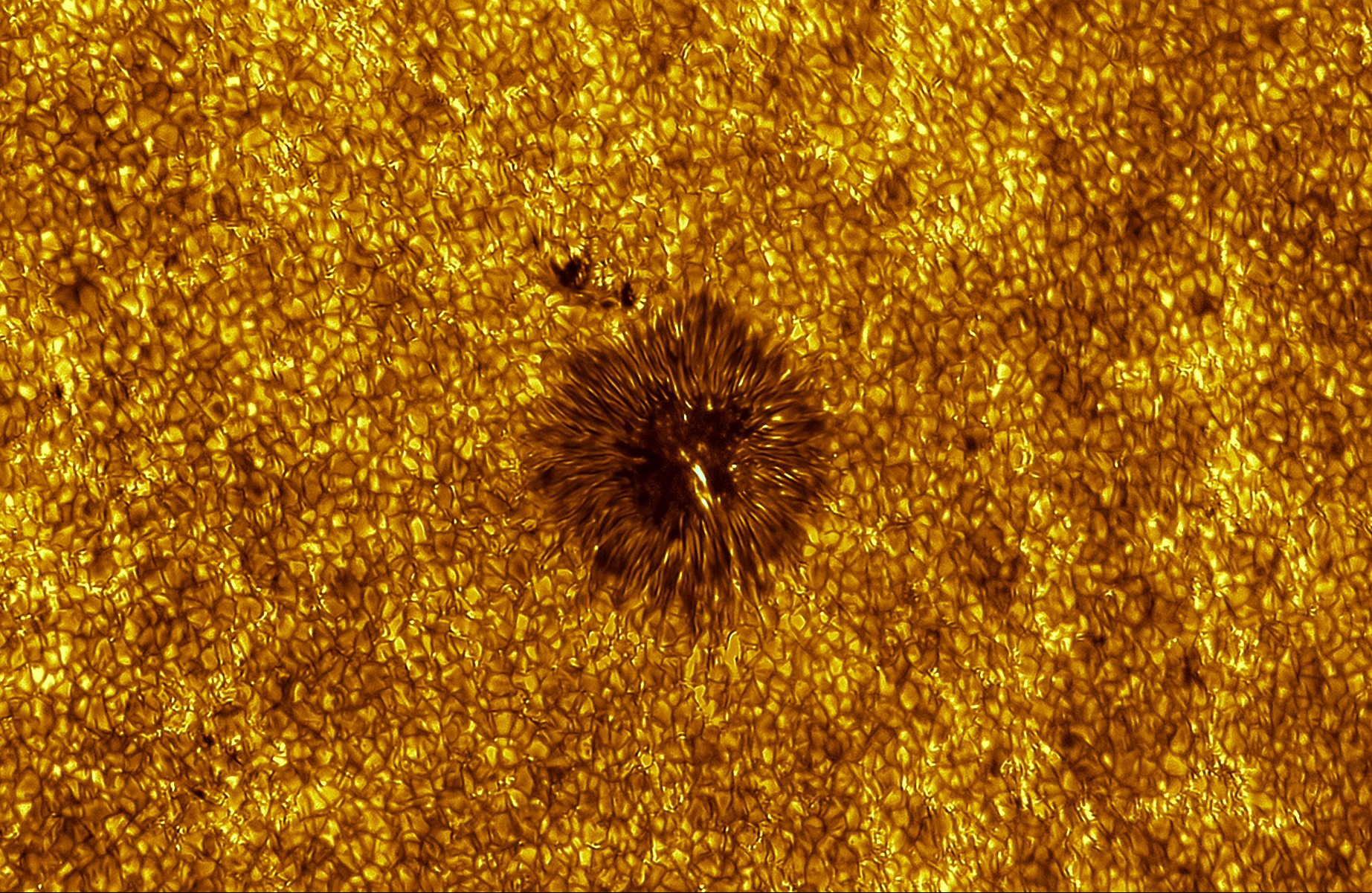 Close-up of the Sun's surface showing a patchwork of glowing convection cells around a dark sunspot