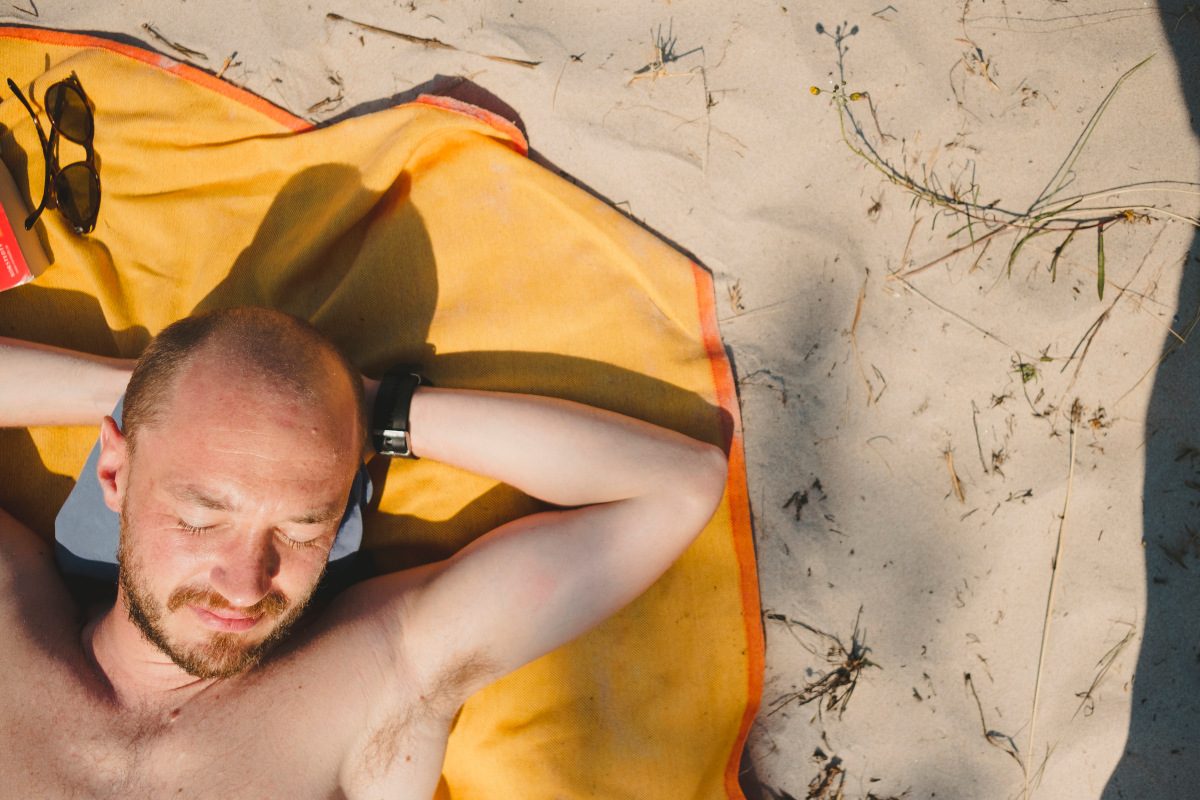 Top down image of a balding man sunbathing on the beach