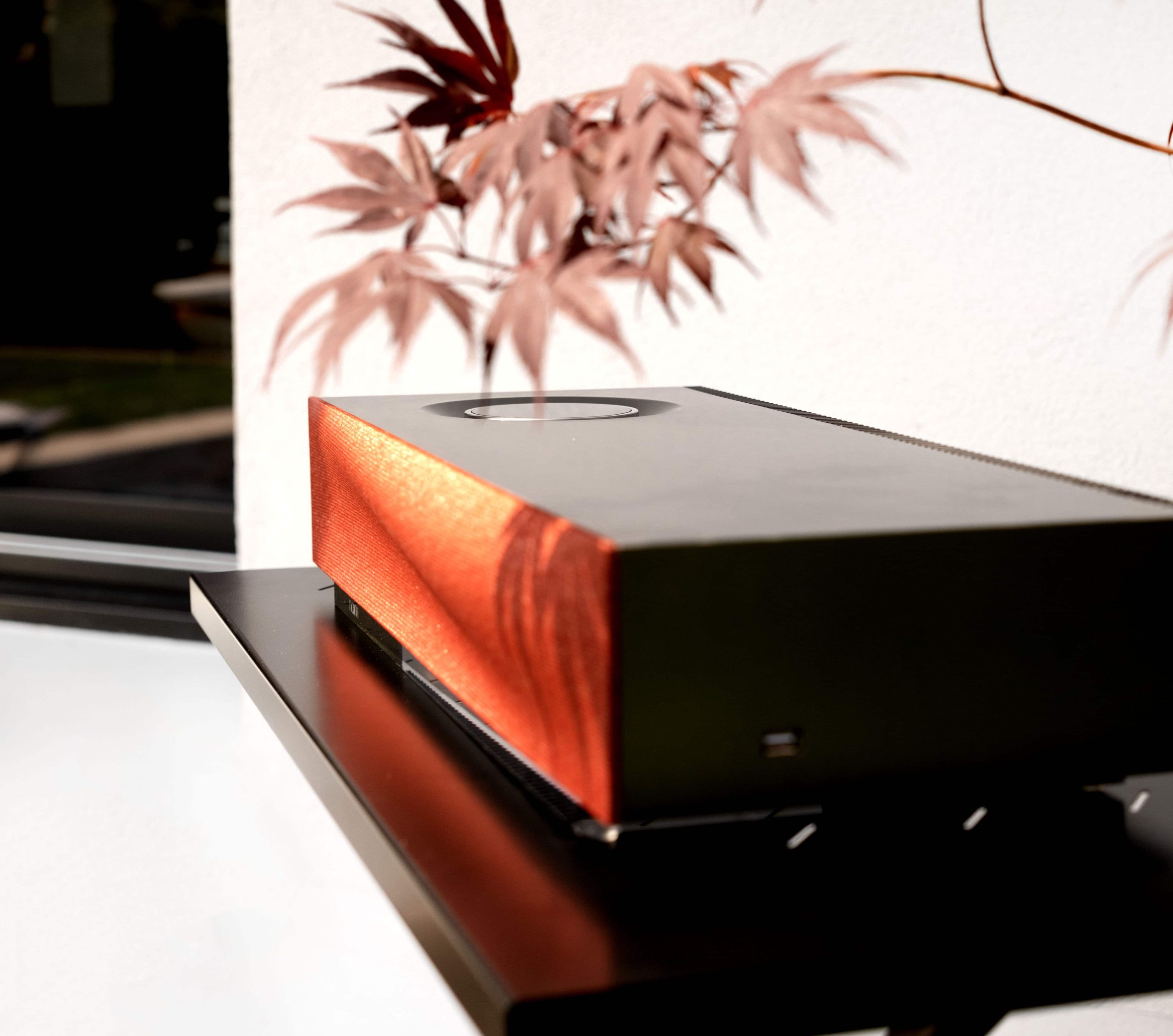 Sleek orange and black audio system on a black table with a houseplant in the background