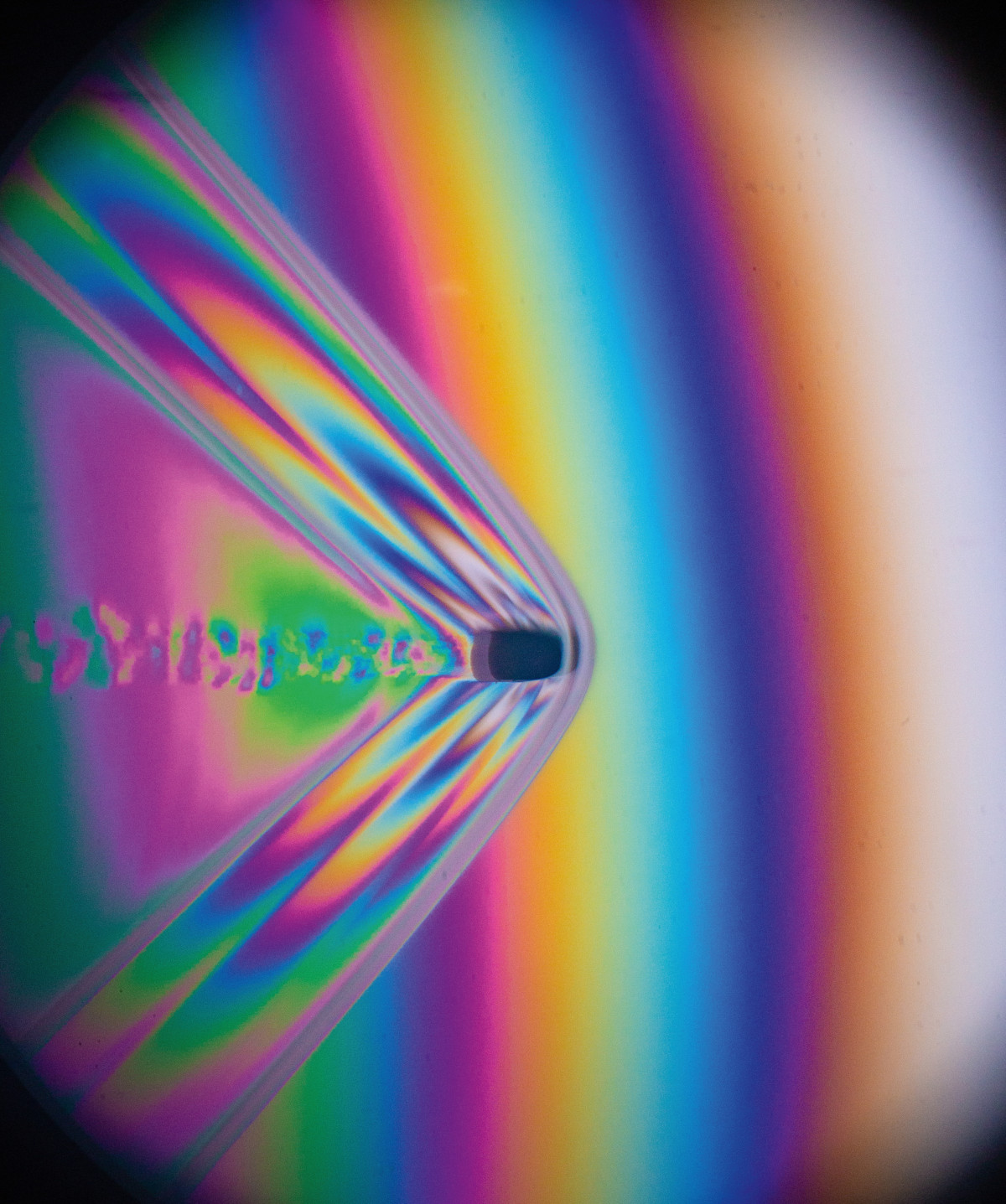 A .22 caliber bullet fired from a rifle flies through the air. This image uses polarizing interferometry to show difference in air pressure, represented by different colors of light. The clear bow wave in front of the bullet shows that it is moving faster than the speed of sound. The exact velocity of this supersonic bullet can be calculated from measurements of the bow wake angle. This image freezes the motion by using a high speed flash with a duration of 1/2,000,000th of a second.